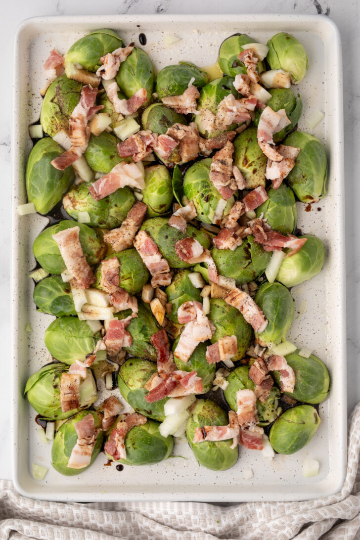 an overhead photo of raw brussels sprouts on a tray with bacon
