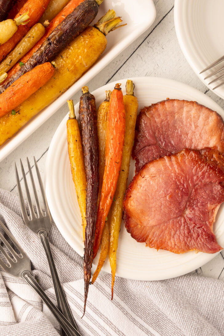 a photo of roasted rainbow carrots on a white plate with slices of ham