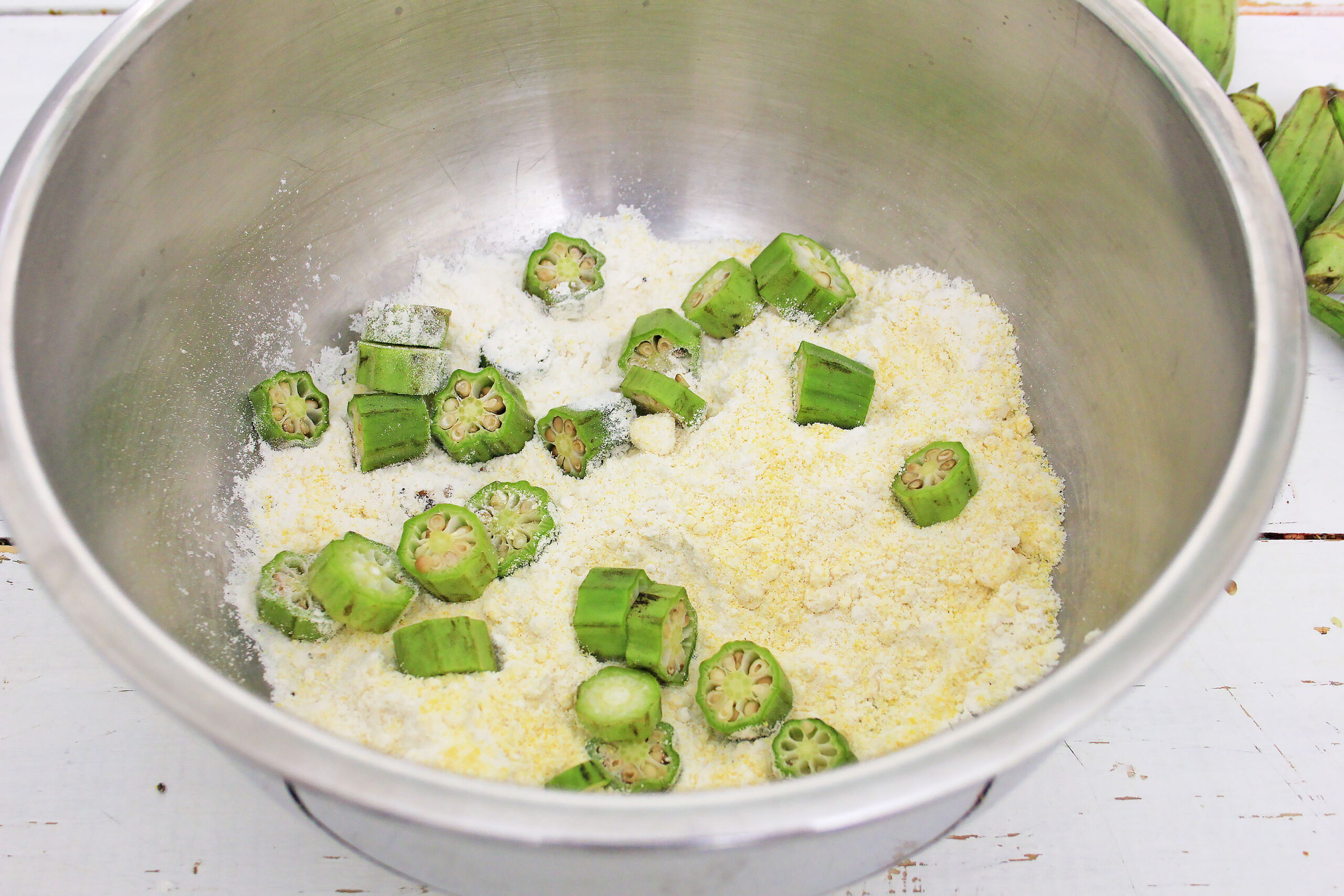 A photo of cut okra being tossed in batter