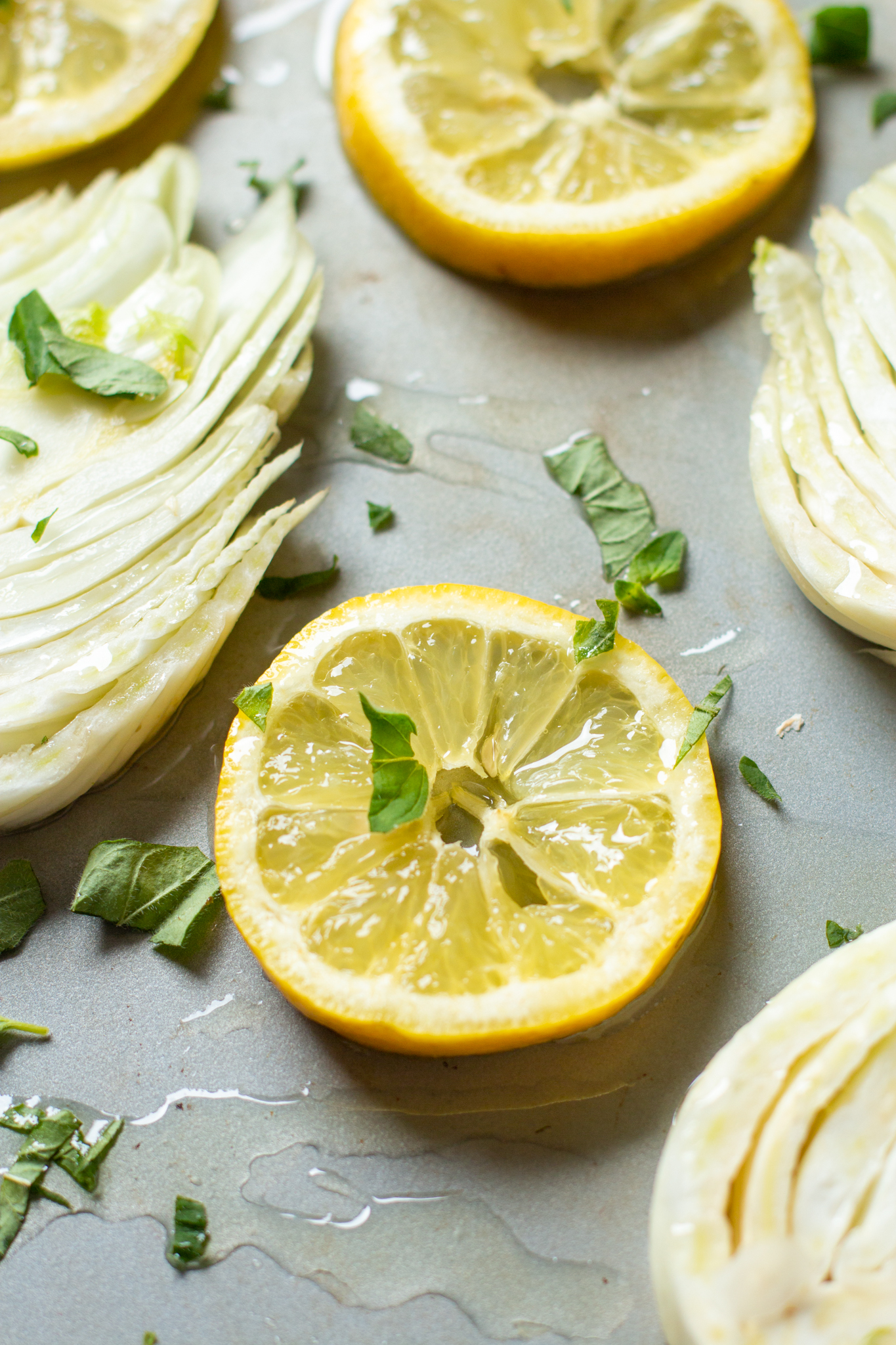 a photo of a slice of lemon and fennel on a baking sheet with herbs