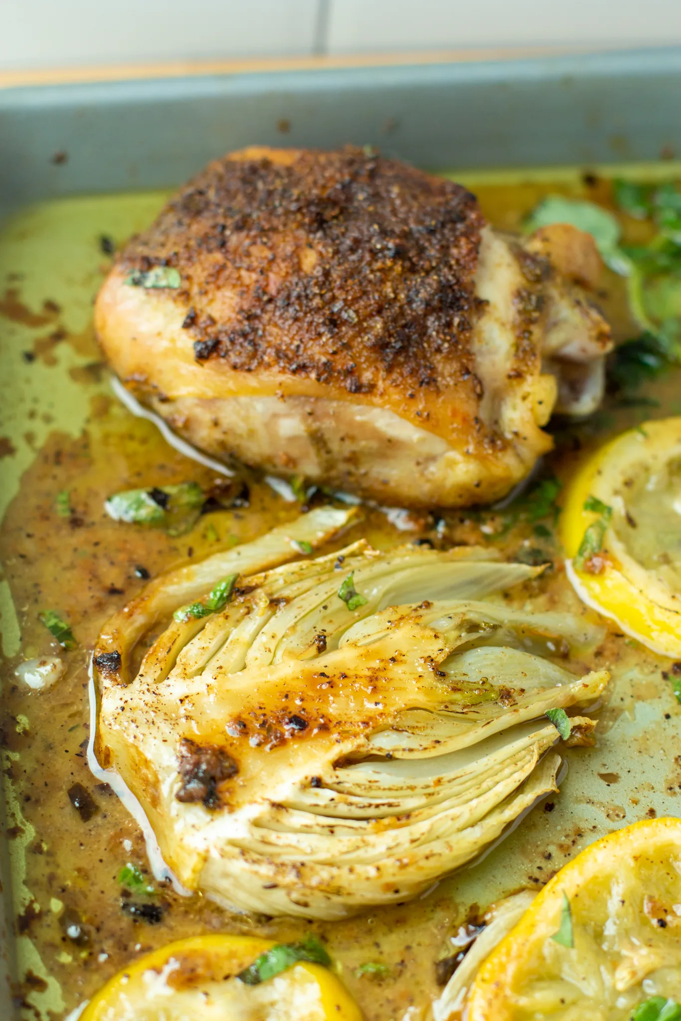 a photo of a roasted chicken thigh and roasted fennel on a baking sheet 
