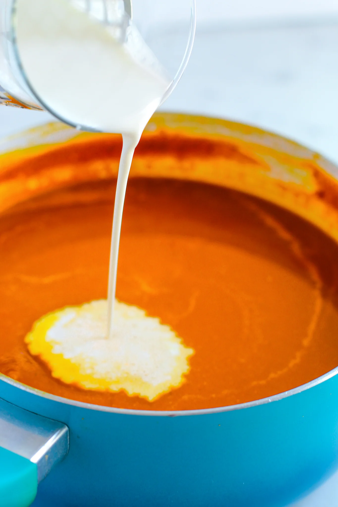A photo of cream being poured into pumpkin soup base