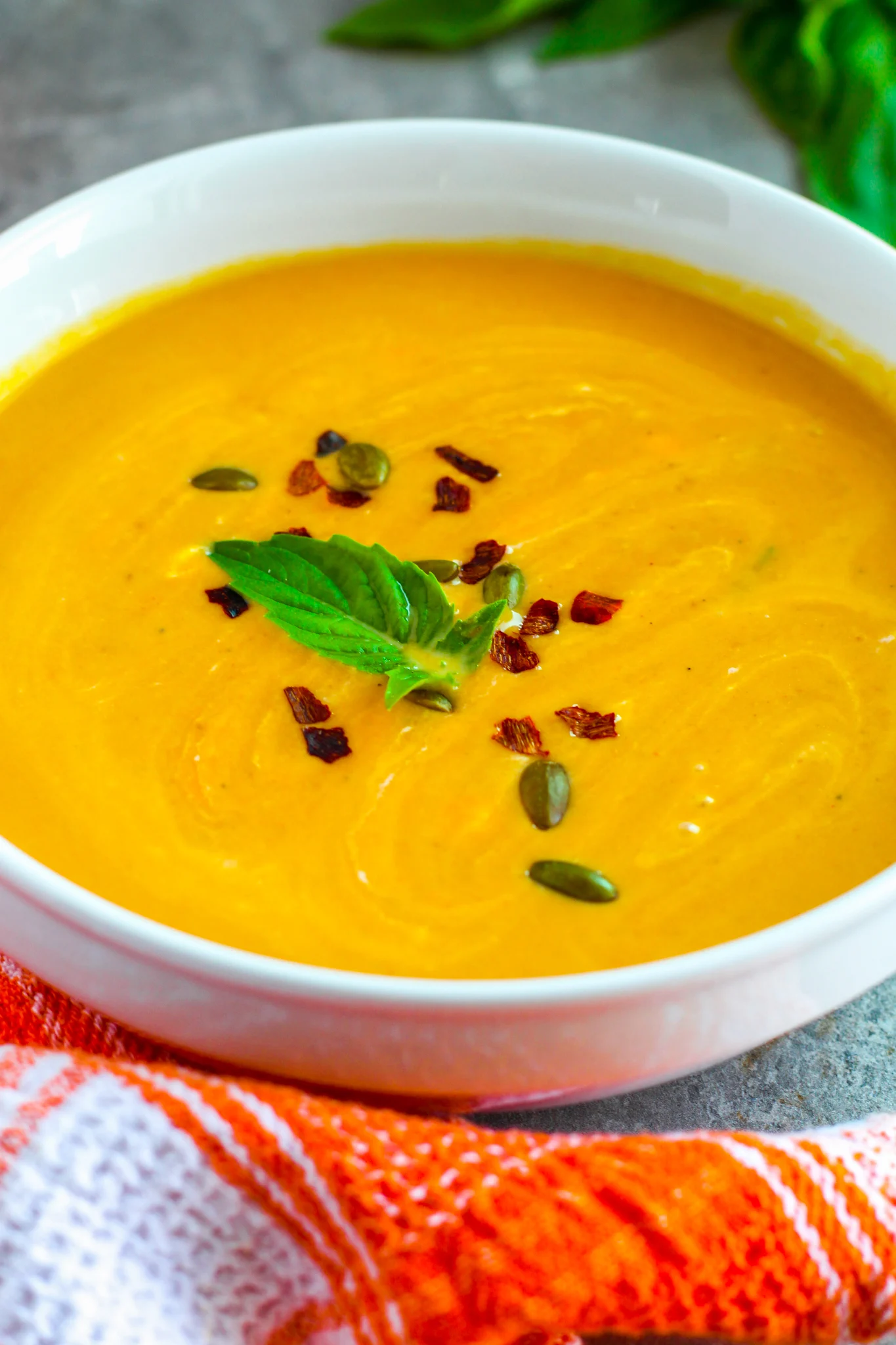 A photo of pumpkin soup in a bowl garnished with a basil leaf