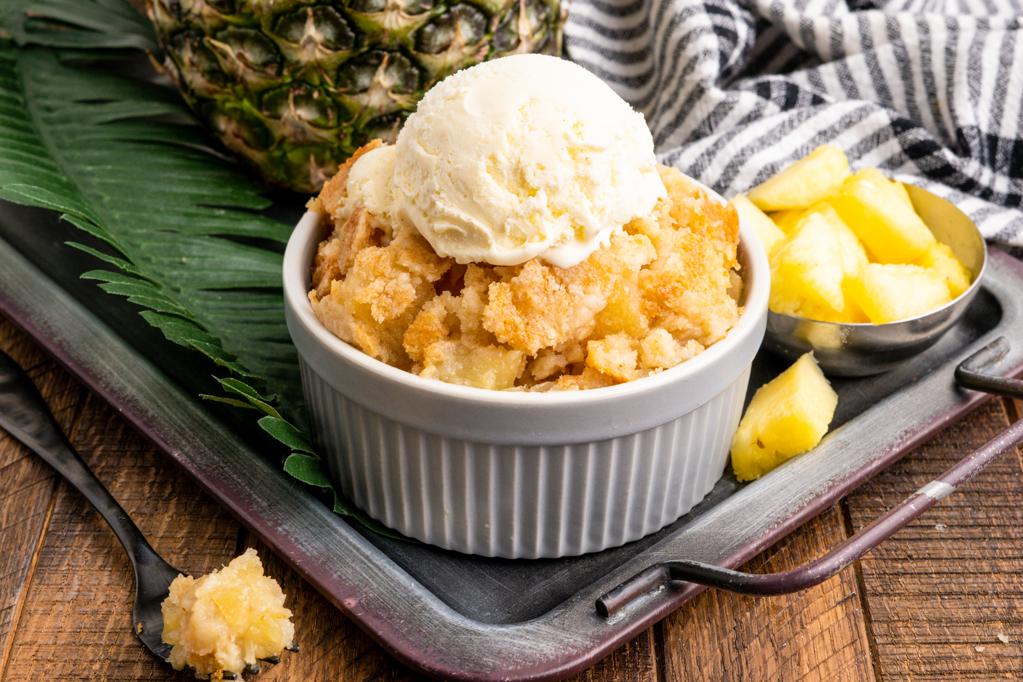 A photo of pineapple dump cake in a small serving dish with ice cream on top
