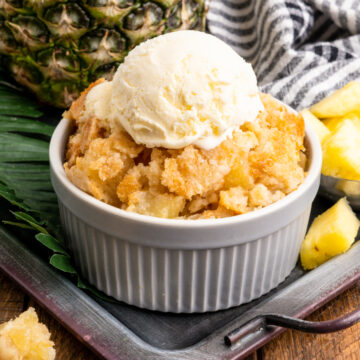 A close up photo of pineapple dump cake in a dish topped with ice cream