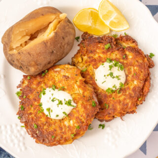 an overhead photo of crab cakes topped with aioli and fresh herbs, with lemon wedges and a baked potato
