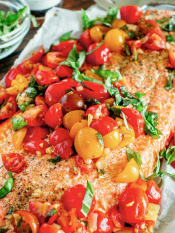 a close up photo of roasted salmon topped with tomatoes and basil