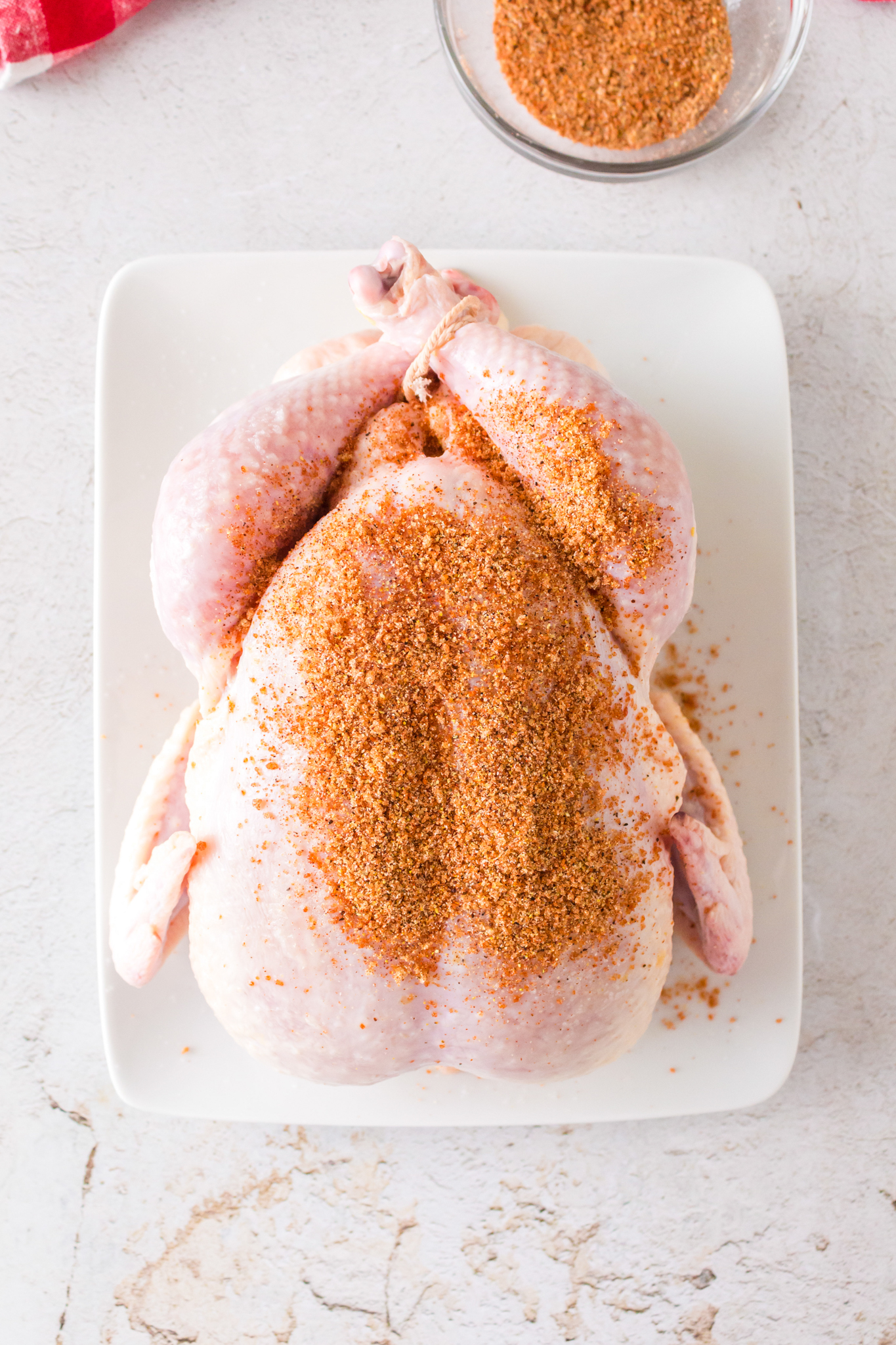 a photo of a raw whole chicken being rubbed with a spice rub