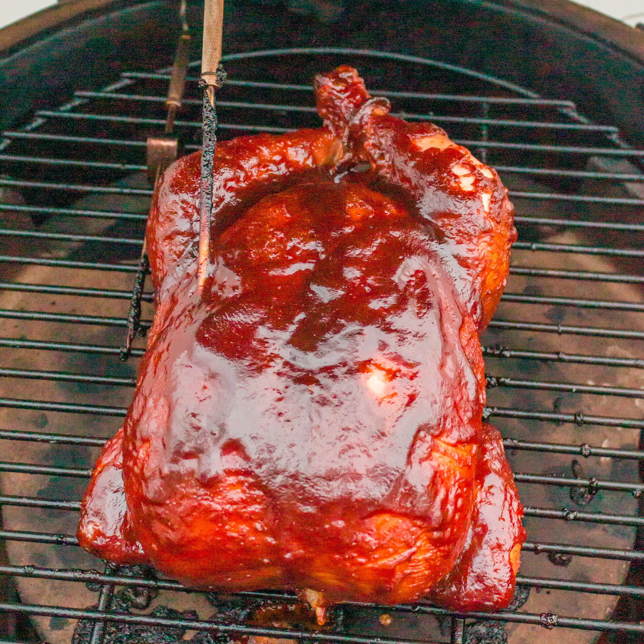 a photo of a whole chicken on a smoker with bbq sauce