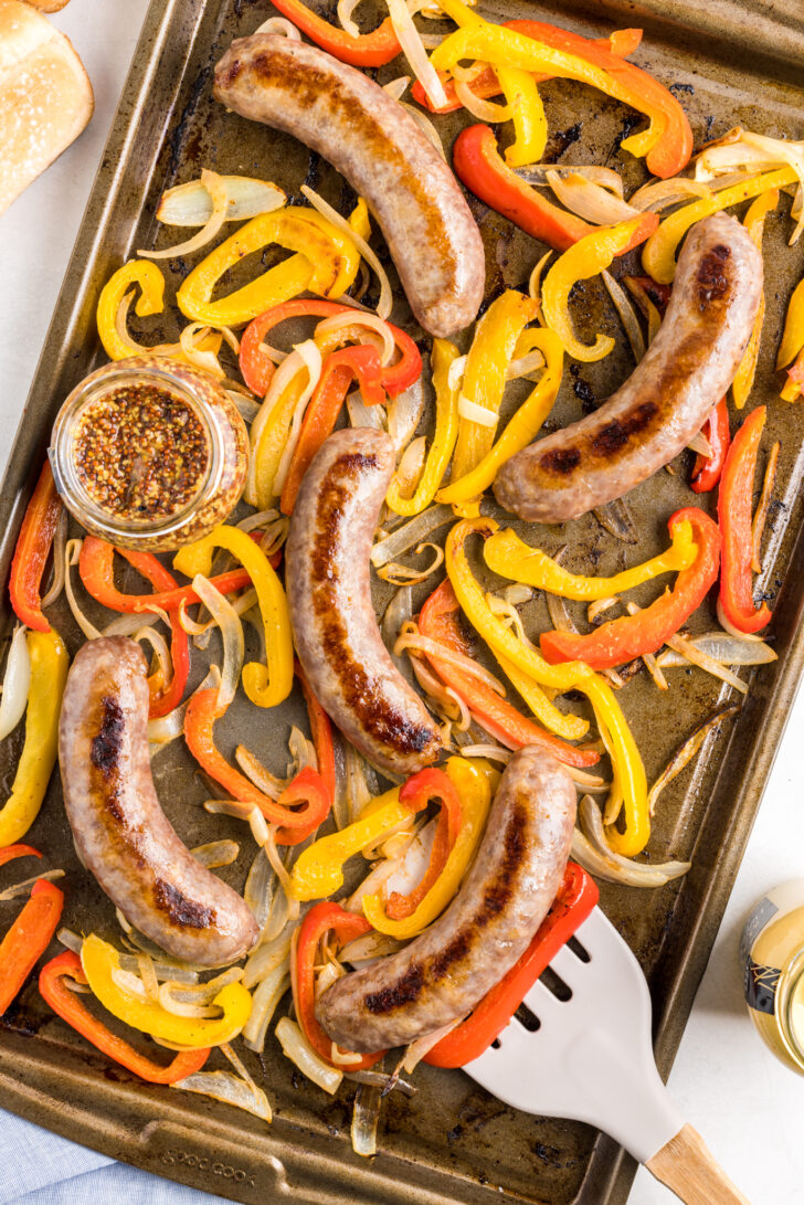 an overhead photo of roasted brats, peppers and onions on a sheet pan
