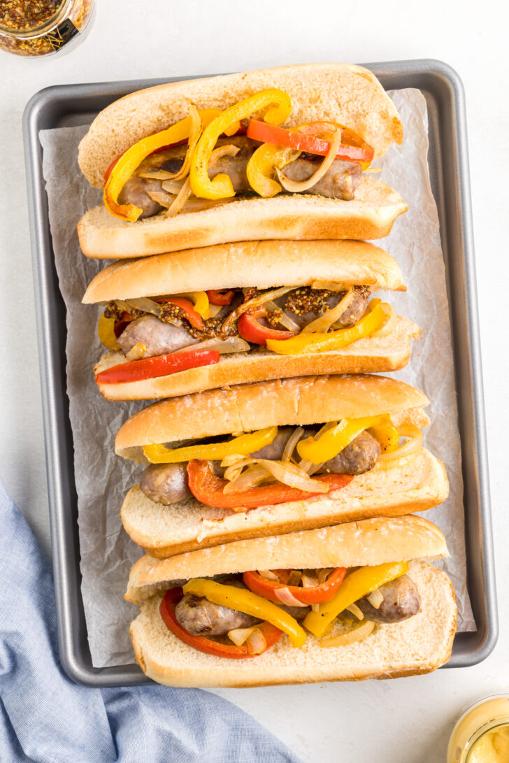 a photo of bratwurst, peppers and onions on buns