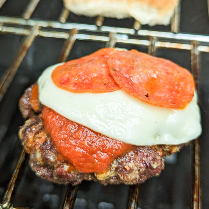 a photo of a pizza burger topped with cheese and pepperoni on a grill