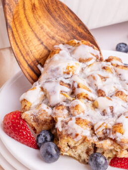 a photo of a wooden spoon serving a slice of cinnamon roll casserole onto a white plate