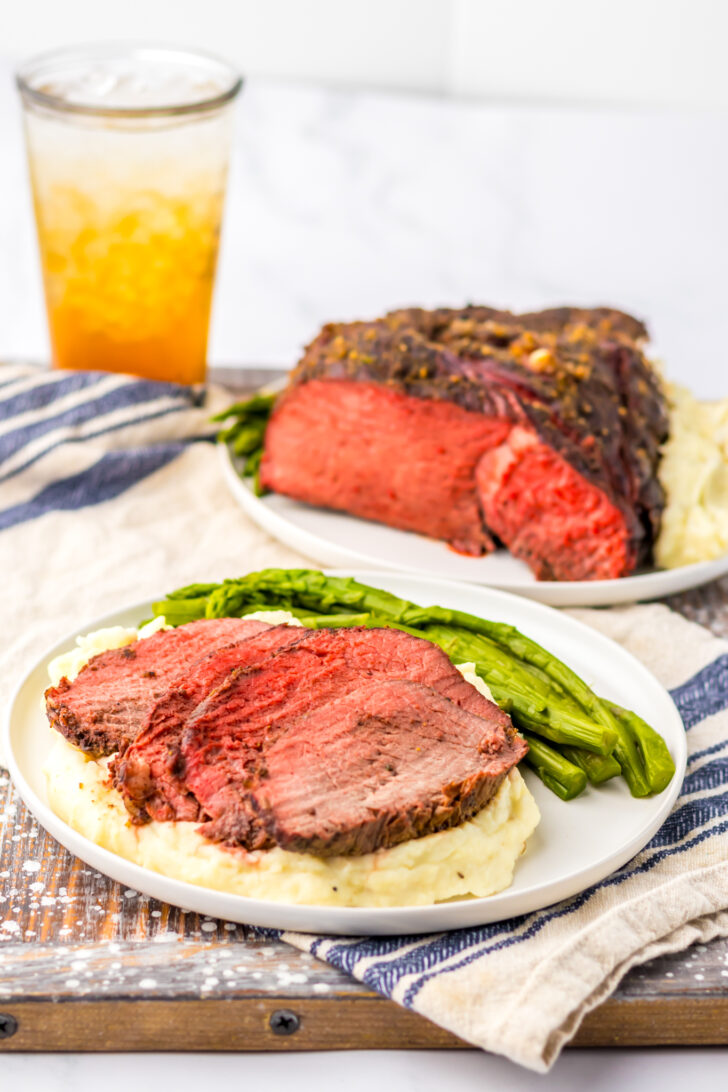 a photo of sliced sirloin tip roast on mashed potatoes with asparagus