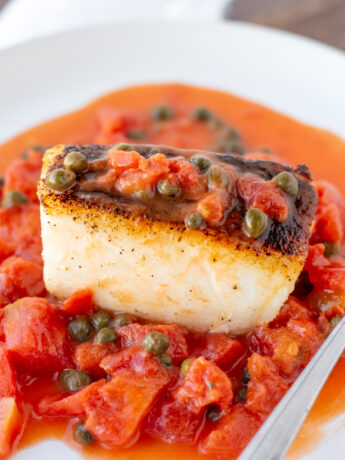 a photo of a seared sea bass filet covered with a tomato caper sauce
