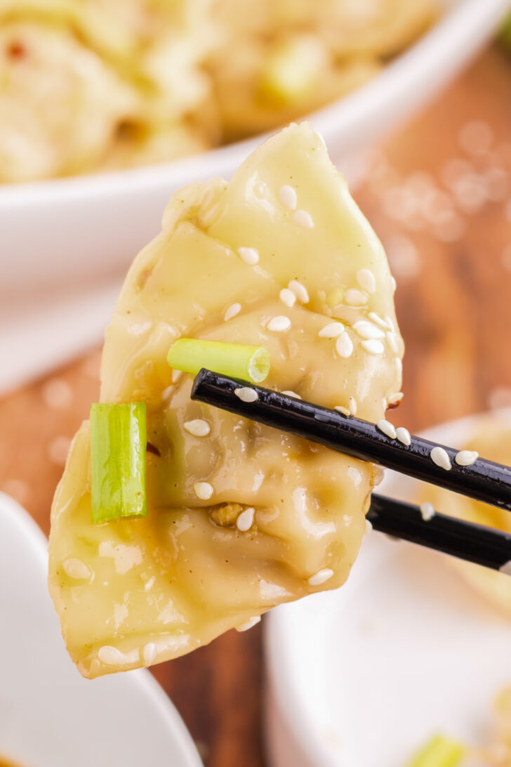 a photo of a wonton being held by black chopsticks