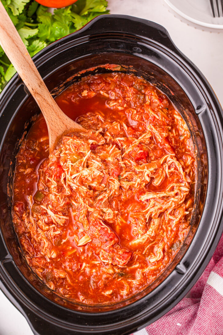 a photo of salsa chicken in a slow cooker with a wooden spoon