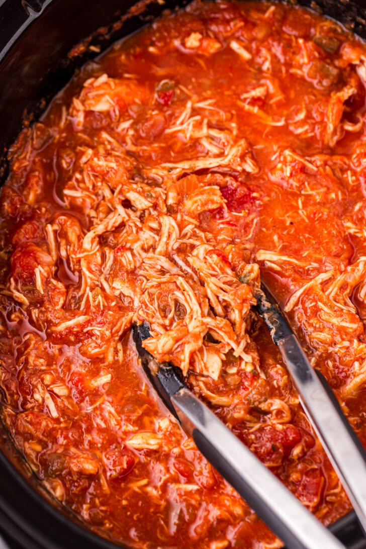 a photo of crockpot shredded chicken being picked up by a set of tongs 