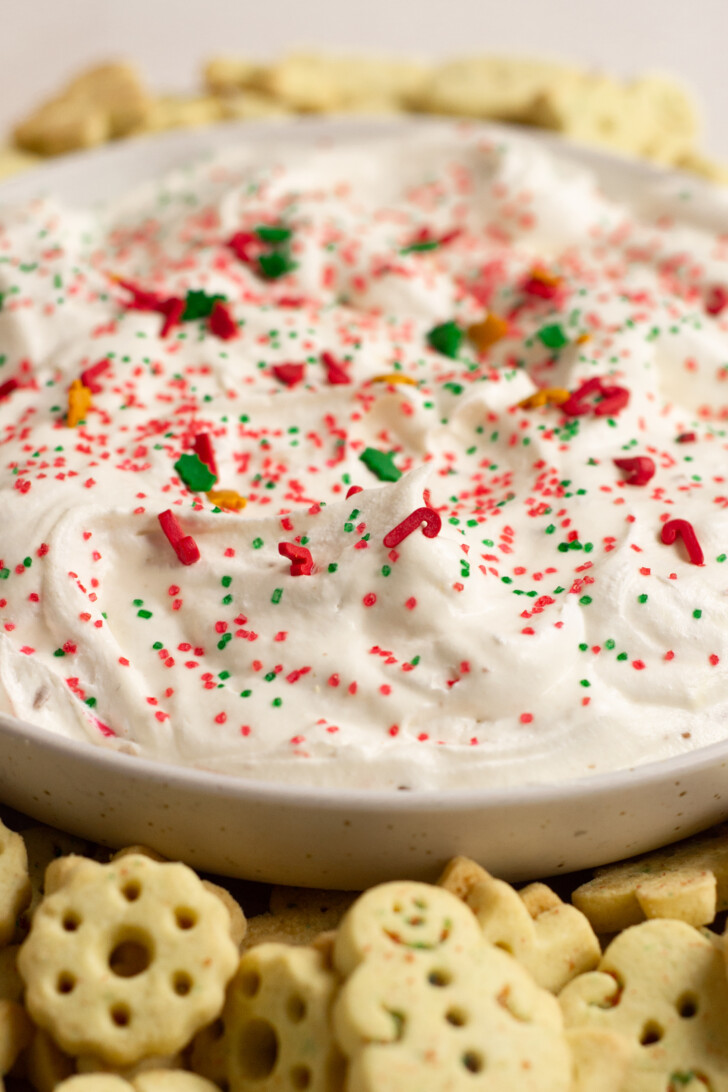 White bowl of Christmas sugar cookie dip with little cookies around it.