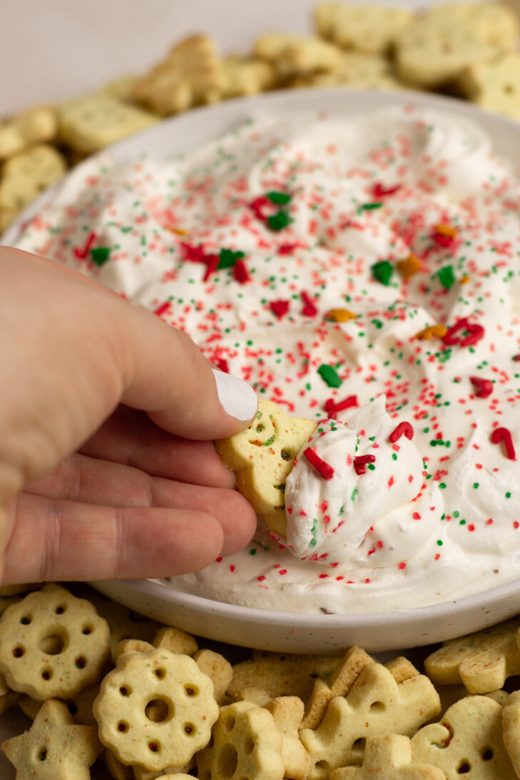 Hand dipping a little sugar cookie into the Christmas sugar cookie dip.