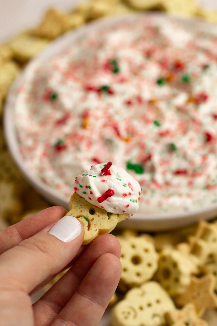 Hand holding a cookie that was dipped into a sugar cookie dip.