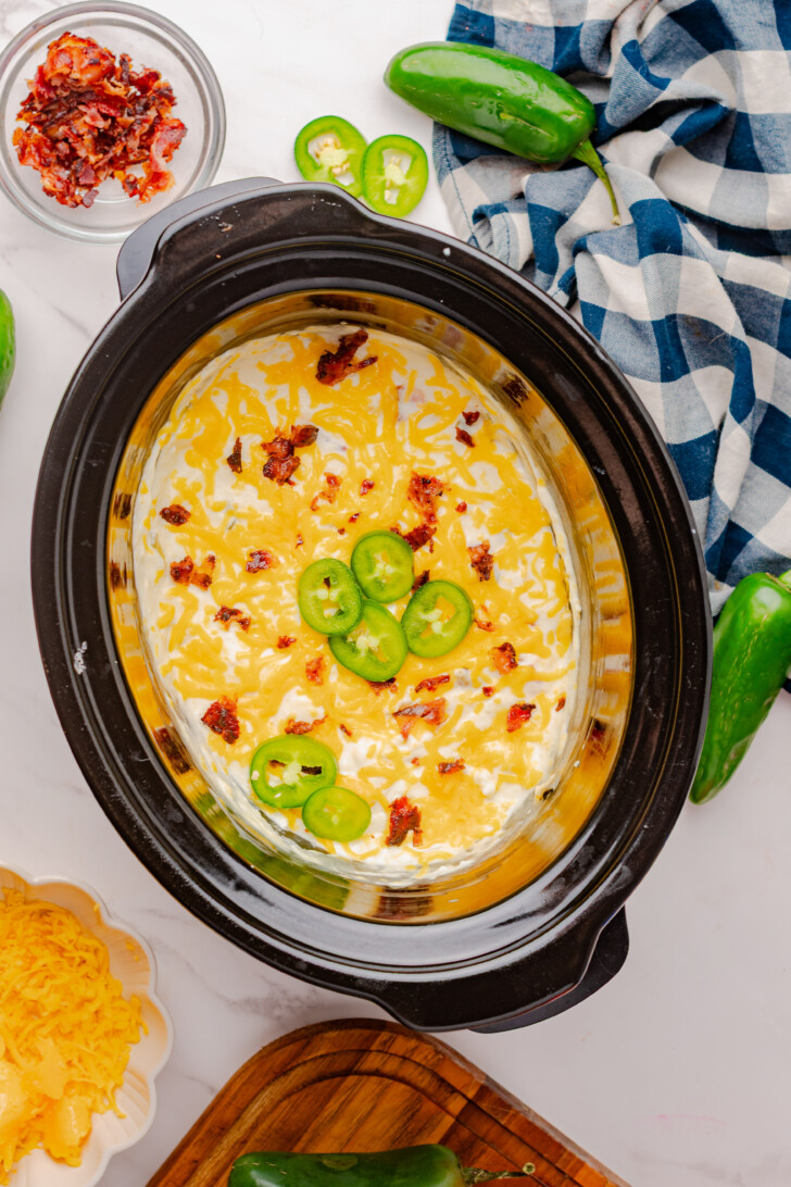 Jalapeno Popper Dip in a Crockpot topped with bacon, cheese and sliced jalapenos