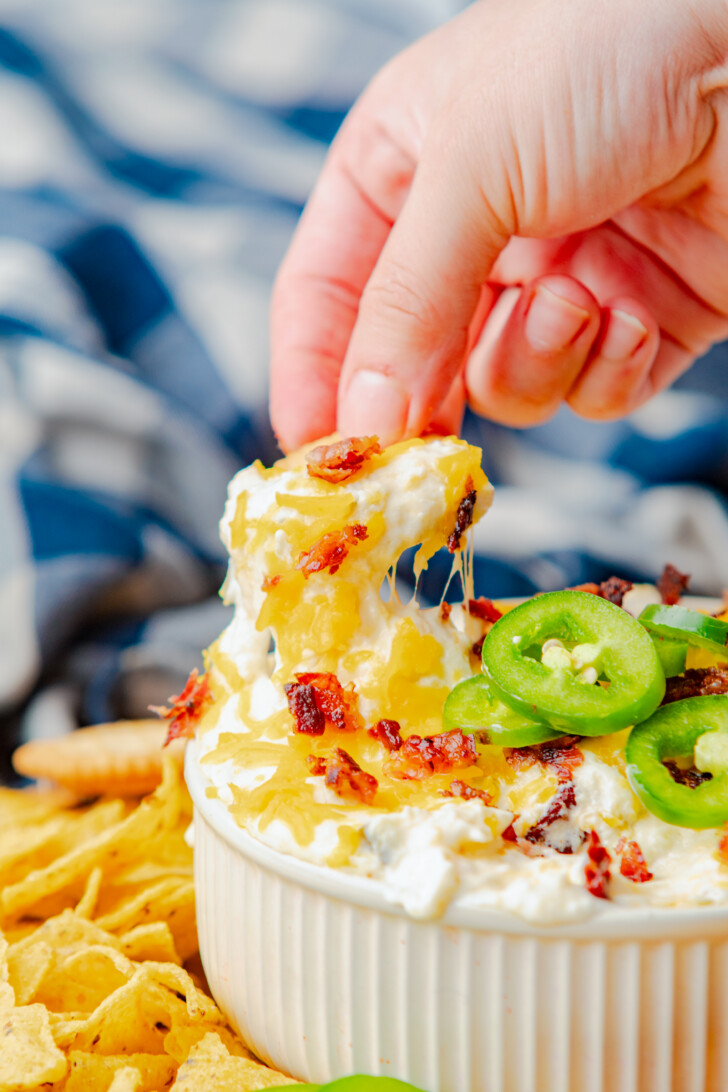 a tortilla chip being dipped iin jalapeno poper dip