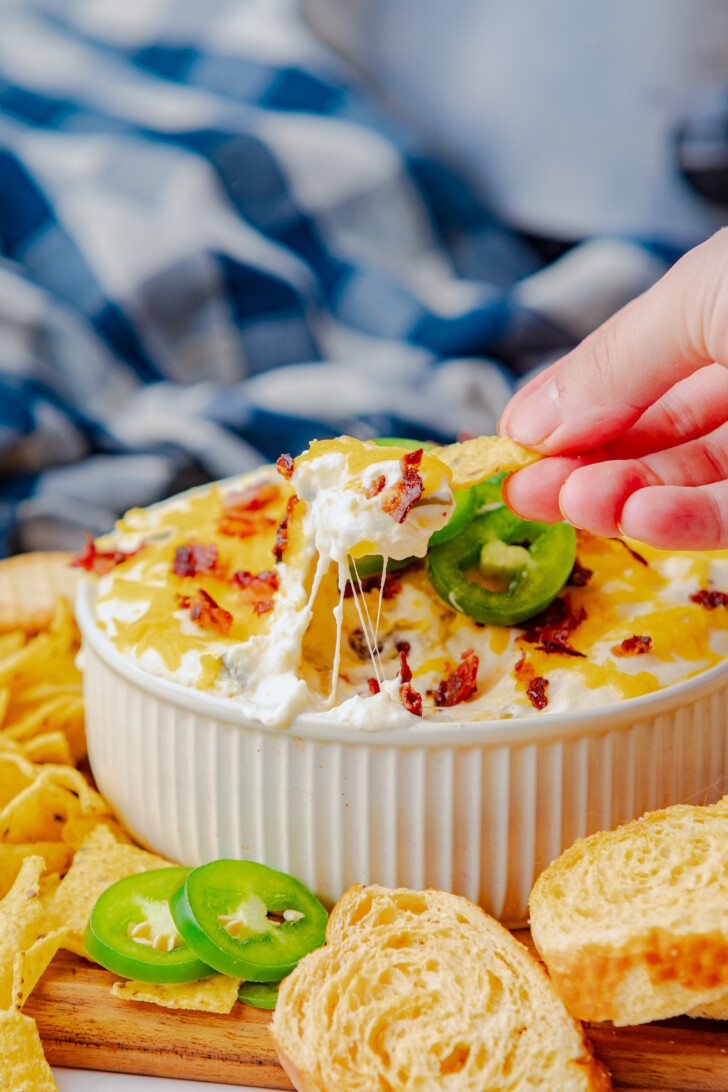a hand dipping a cracker into a cheesy dip