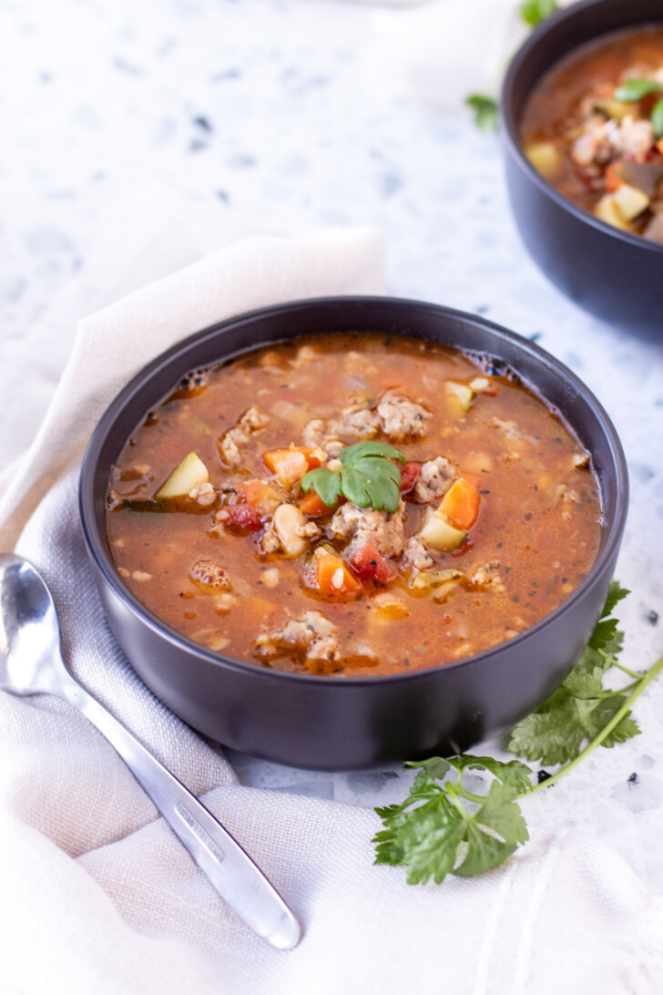 a black bowl filled with italian sausage soup