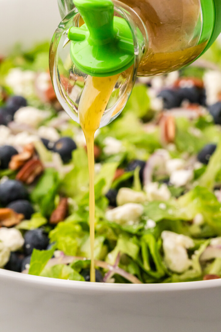 dressing being poured over a green lettuce salad with feta