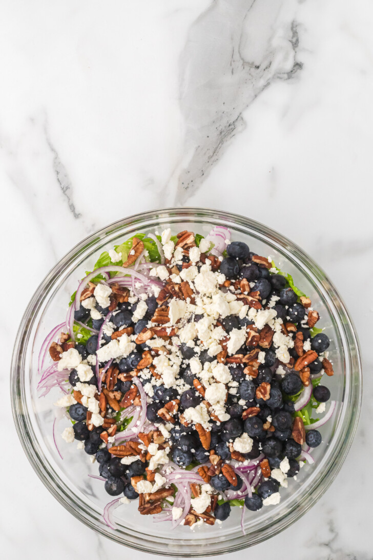 a salad in a bowl with blueberries, feta and pecans