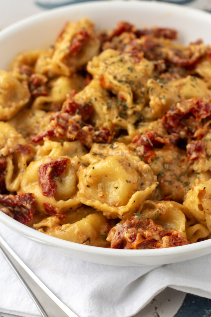 a white bowl filled with creamy tomato tortellini