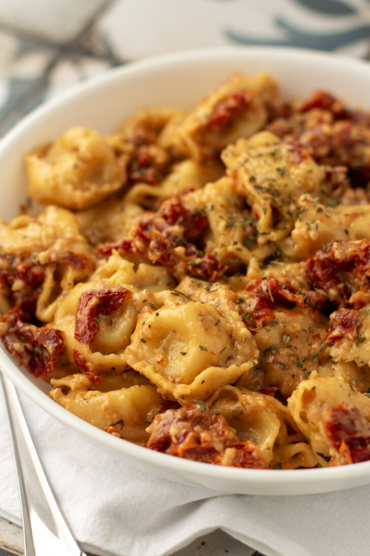 a white bowl filled with tortellini and sun dried tomatoes