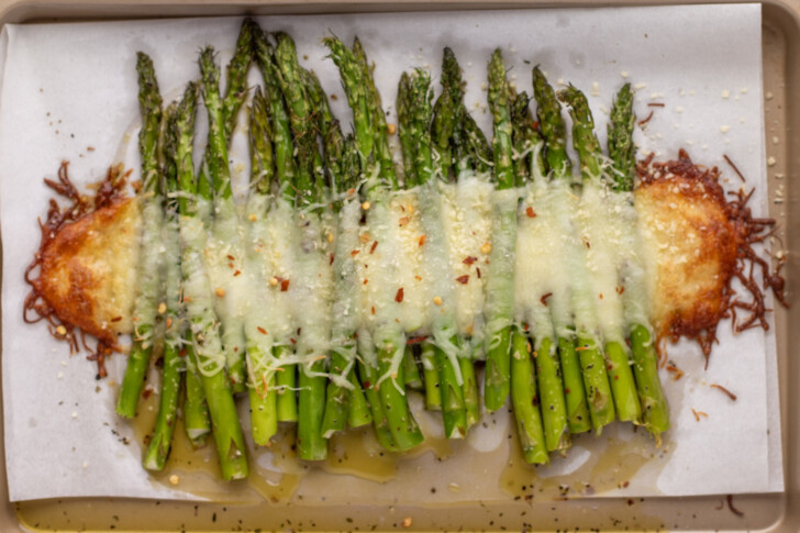a baking tray lined with parchment paper with asparagus spears and cheese