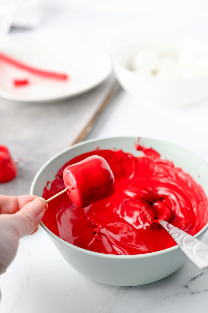 a marshmallow being dipped in melted red candy