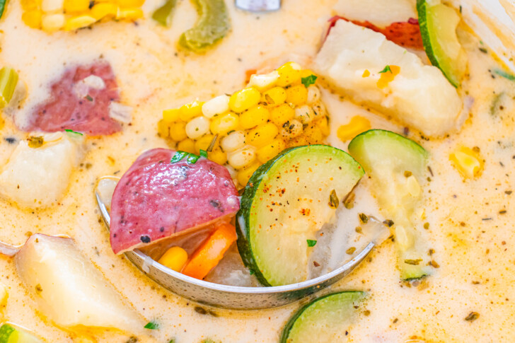 a close up photo of a soup with potatoes, corn and zucchini on a spoon