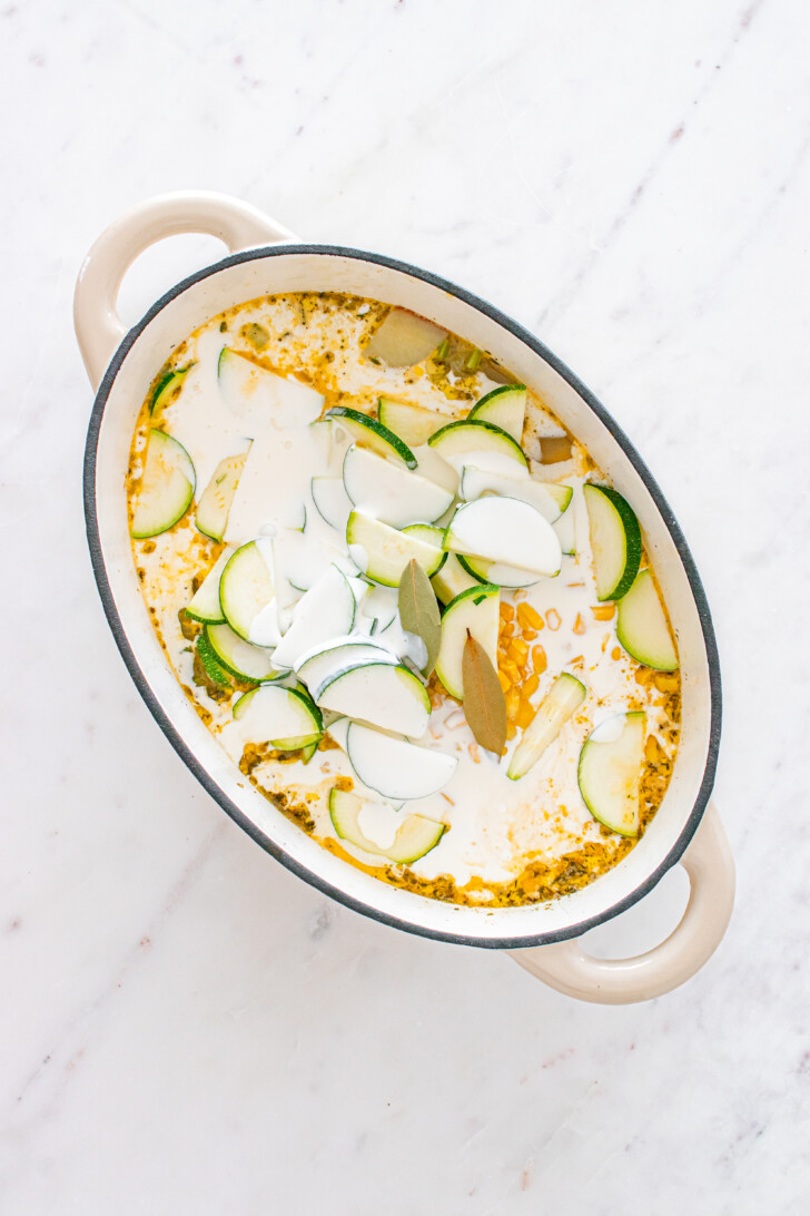 heavy cream and zucchinis being added to a soup in a dutch oven