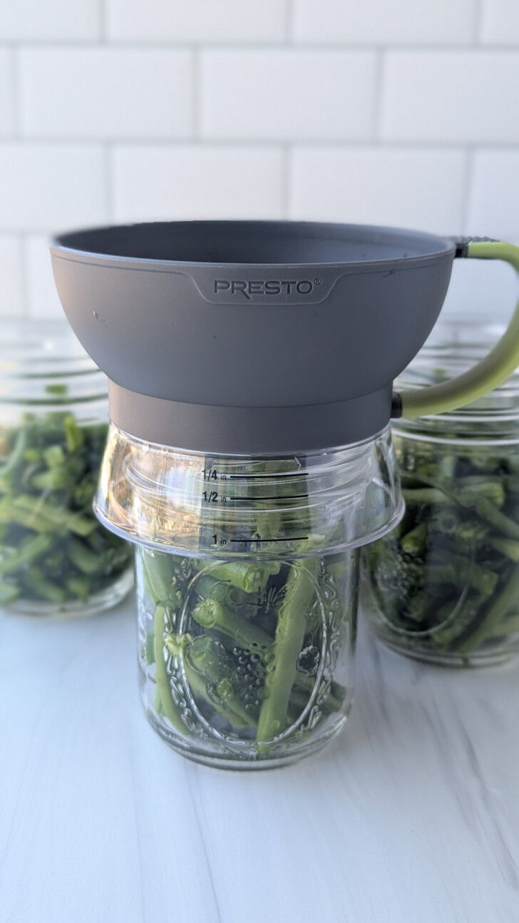 a funnel being used to filled a jar of green beans for canning