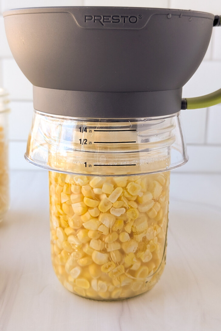 a jar with a funnel on top being filled with sweet corn kernsl