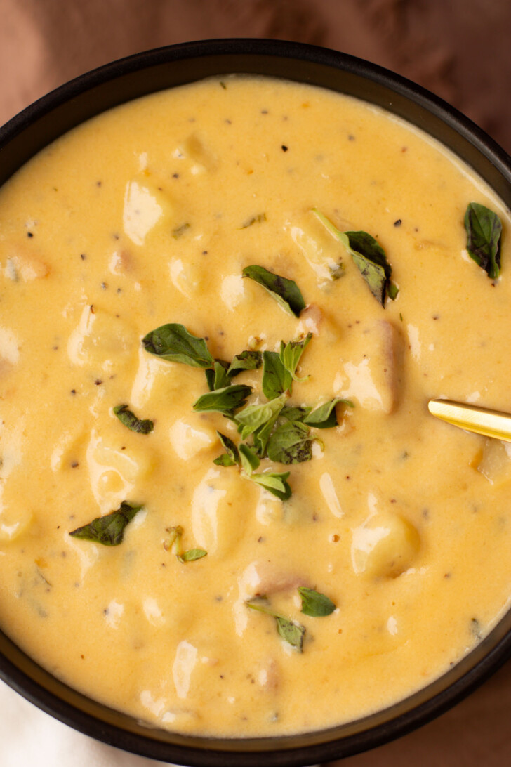 cheesy ham and potato soup in a black bowl topped with green herbs
