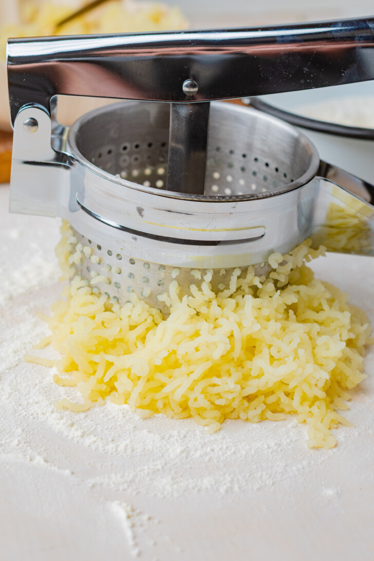 cooked potato being put through a potato ricer